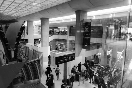 Téléchargez les photos : Paris, France - Juillet 2019 - Passagers transportant leurs bagages et utilisant des escaliers roulants dans un hall de la gare de l'aéroport Roissy-Charles de Gaulle, doté d'un puits léger et de piliers en béton - en image libre de droit