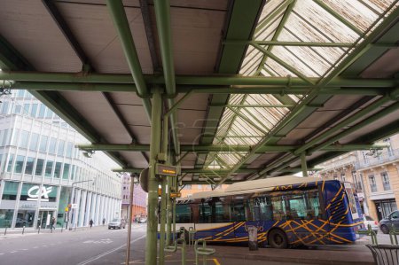 Foto de Toulouse, Francia - Dic. 2020 - Un autobús urbano operado por Tisseo, bajo el dosel de metal y vidrio de la estación de autobuses de Jeanne D 'Arc, frente al edificio de cristal de una sucursal bancaria de Crdit Agricole - Imagen libre de derechos