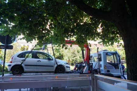 Téléchargez les photos : Toulouse, France - 10 juin 2023 - Une voiture garée illégalement est saisie par les services municipaux : elle est remorquée au moyen d'une grue sur un camion, soulevée avec des câbles attachés aux roues - en image libre de droit