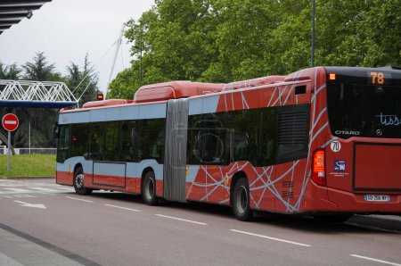 Photo for Toulouse, France - June 1, 2023 - A red, articulated city bus operated by transportation company Tisseo, arrives by Edouard Belin Avenue in front of CNES (French Space Agency), on Rangueil Campus - Royalty Free Image