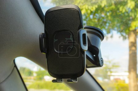 Photo for A system of universal phone mounting for car, fixed at the windscreen, with a suction cup, in front of the driver's seat ; the holder features a hinged arm and lateral clamps to tighten the device - Royalty Free Image