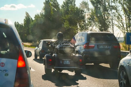 Foto de Autoroute A68, Francia - Agosto de 2020 - Una escena inusual en Francia, con, entre otros vehículos, una gran motocicleta Harley-Davidson de tres ruedas, con una bandera estadounidense, conducida por un fan de Johnny Hallyday - Imagen libre de derechos