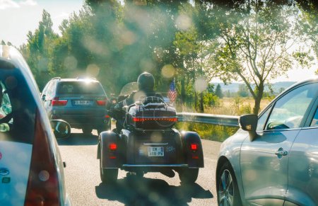 Téléchargez les photos : Autoroute A68, France - Août 2020 - Une scène insolite en France, avec, entre autres véhicules, une grande moto Harley-Davidson à trois roues, battant pavillon américain, conduite par un fan de Johnny Hallyday - en image libre de droit
