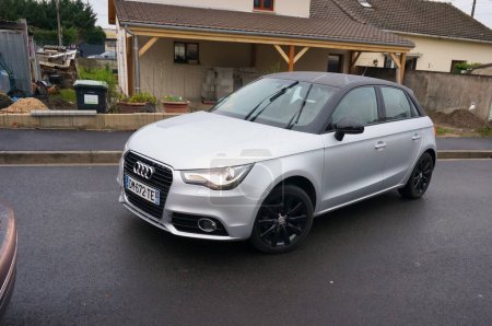 Photo for Val-d'Oise, France - Dec. 2017 - A small compacf gray Audi A1 of the German carmaker Volkswagen, with headlights on and windscreen wipers activated on a rainy day, in a reverse manoeuver - Royalty Free Image