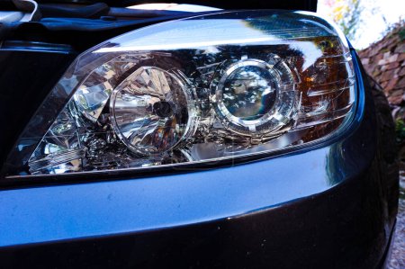 Téléchargez les photos : Vue rapprochée d'un phare de voiture, y compris le clignotant orange, avec des ampoules à l'intérieur et des surfaces réfléchissantes, sur un châssis bleu métallique foncé (ou gris bleuâtre foncé) - en image libre de droit