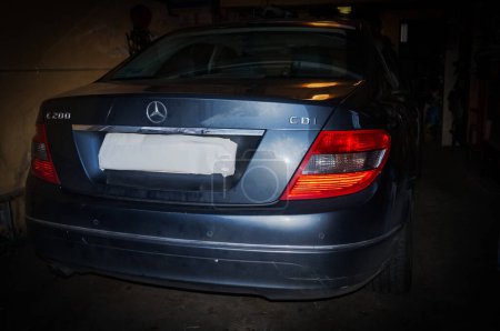 Foto de Albi, Francia - Marzo 2020 - Premium coche ejecutivo alemán protegido a la sombra en un garaje; vista trasera de un gris oscuro 2010-Mercedes C200 con una barra de cromo en el maletero y una placa de matrícula oculta - Imagen libre de derechos