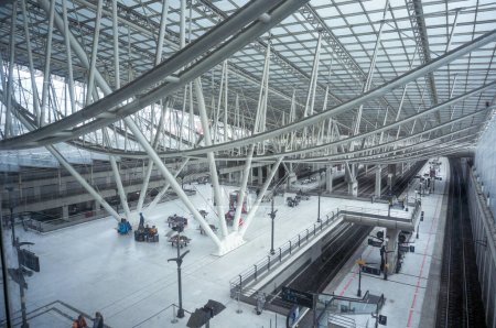 Foto de Aeropuerto París-Roissy-Charles de Gaulle, Francia - Julio 2019 - Hall en la estación de tren, por encima de la plataforma de la estación y las vías y bajo un enorme marco metálico, con los pasajeros esperando - Imagen libre de derechos