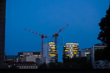 Téléchargez les photos : Paris, France - Sept. 2020 - Vue de nuit du chantier de bâtiments résidentiels futuristes en construction avec deux grues à tour et des reflets du coucher du soleil, dans le quartier moderne de Bercy - en image libre de droit