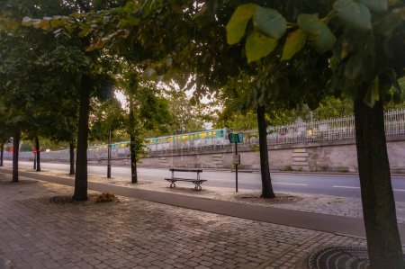 Téléchargez les photos : Paris, France - Sept. 2020 - Vue paisible de l'aube, prise sous les arbres de la bordure verdoyante du boulevard de Bercy, au crépuscule ; en arrière-plan, un métro passe sur le pont - en image libre de droit