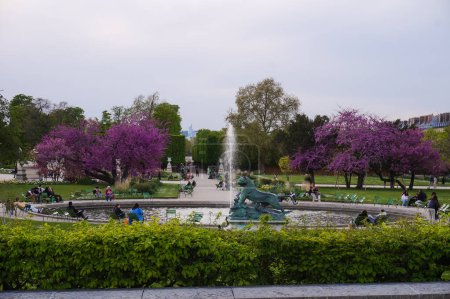 Téléchargez les photos : Paris, France - Avril 2022 - Les habitants se reposent et se refroidissent dans le parc, autour d'une fontaine à jet d'eau, des arbres à fleurs violettes, dans les jardins des Tuileries, dans le 1er arrondissement de la capitale - en image libre de droit