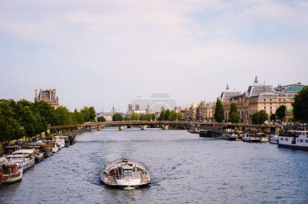Photo for Paris, France - View on the river Seine with a sightseeing bateau-mouche cruising and barges by the docks, the Leopold Senghor Bridge, Orsay Museum and Notre Dame Cathedral in the backround - Royalty Free Image