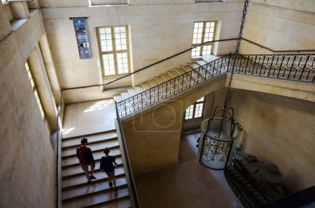 Photo for Paris, France - July 2019 - Monumental staircase inside the Army Museum, in Hotel des Invalides, built with bright stone in a sober classical style, with visitors going up the steps - Royalty Free Image