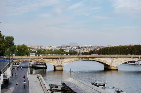Photo for Paris, France - Sept. 2022 - The brige Pont des Invalides, crossing the River Seine ; on the banks, Parisians jogging or strolling by the water and the boats ; Chaillot Palace is visible afar - Royalty Free Image