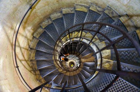 Photo for Spiral staircase with metal handrail and many steps, in form of ammonite when seen from above ; somebody lower going down the stairs - Royalty Free Image