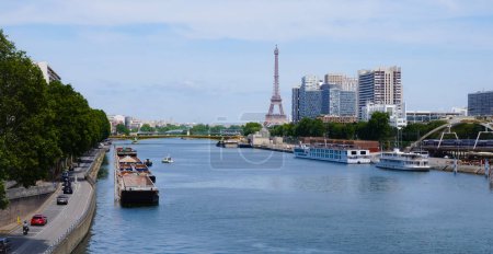 Foto de París, Francia - junio 2020- El río Sena, por delante de la Torre Eiffel y los edificios de los distritos de Front-de-Seine y Beaugrenelle, construidos a orillas del río, con barcazas y cruceros en el puerto de Javel - Imagen libre de derechos