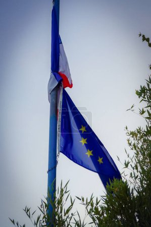 Foto de Banderas de Francia y de la Unión Europea a media asta, marcadas como "Municipio de Le Sequestre", enredadas alrededor del asta de la bandera y ondeando en el viento; ilustración del declive francés y europeo - Imagen libre de derechos