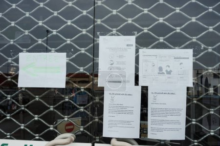 Foto de Albi, Francia - 20 de marzo de 2020- Storefront cerrado con un obturador metálico debido a la contención; instrucciones oficiales y carteles sobre la pandemia de Covid-19 se muestran en la ventana de vidrio - Imagen libre de derechos