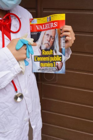 Foto de Marsella, Francia - Mayo 2020 - Un médico en blusa blanca señala con el dedo a una revista que presenta a Pr Didier Raoult, el famoso investigador que aboga por el protocolo "HCQ + AZT" (foto puesta en escena) - Imagen libre de derechos