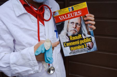 Téléchargez les photos : Marseille, France - Mai 2020 - Un médecin en chemisier blanc pointe du doigt un journal mettant en vedette le Pr Didier Raoult, chercheur de renommée mondiale préconisant le protocole "HCQ + AZT" (photo mise en scène) - en image libre de droit