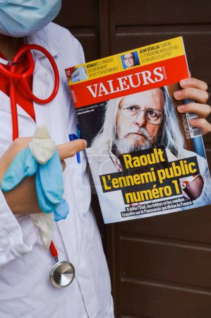 Foto de Marsella, Francia - Mayo 2020 - Un médico en blusa blanca sostiene un número de Valeurs Actuelles con Pr Didier Raoult, un infectólogo conocido por el tratamiento con hidroxicloroquina (foto puesta en escena) - Imagen libre de derechos