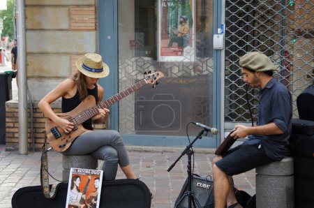 Foto de Toulouse, Francia - 2 de julio de 2023 - Un dúo de dos músicos callejeros, una mujer tocando una guitarra y un hombre tocando un instrumento de viento, interpreta una canción en Rue de Metz, en el distrito histórico de Carmes - Imagen libre de derechos