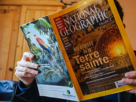 Photo for Tarn, France - Feb. 2019 - A man reads a French edition of the magazine National Geographic devoted to the Holy Land and featuring the golden cupola of the Dome of the Rock Mosque in Jerusalem - Royalty Free Image