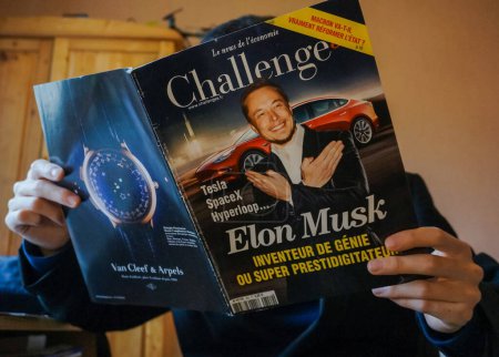 Téléchargez les photos : Tarn, France - Février 2019 - Un homme lit un numéro du journal économique français Challenges montrant l'homme d'affaires Elon Musk devant une Tesla, avec une publicité pour une marque de montres de luxe au dos - en image libre de droit