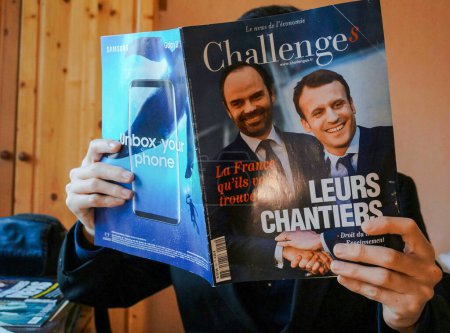 Photo for Tarn, France -Feb. 2019- A man absorbed in an issue of the economic newspaper Challenges whose cover shows French President Emmanuel Macron smiling and shaking Prime Minister Edouard Philippe's hands - Royalty Free Image