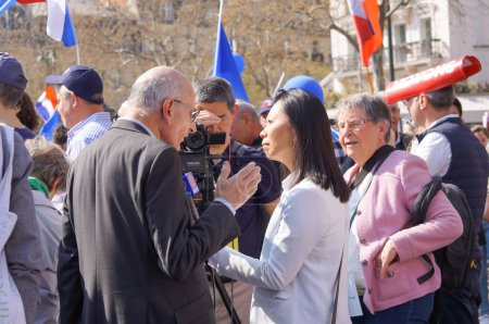 Foto de París, Francia - 27 de marzo de 2022 - Una periodista del canal disidente chino NTD TV (Epoch Times) entrevista a un partidario del candidato presidencial Eric Zemmour, en el gran mitin de Trocadero - Imagen libre de derechos