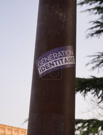 Foto de Albi, Francia - Feb. 2021 - Una pegatina azul y blanca de Generation Identitaire, un movimiento juvenil de derecha que se opone a la invasión migratoria y la islamización de Europa, pegada en un poste de lámpara - Imagen libre de derechos