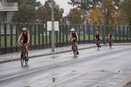 Foto de Reims, Francia - Oct. 2022 - Jóvenes en ropa deportiva en bicicleta de carreras, disputando el Triatlón Stade de Reims en una carretera mojada, bajo la lluvia, frente a la Universidad, en el Campus Moulin de la Housse - Imagen libre de derechos
