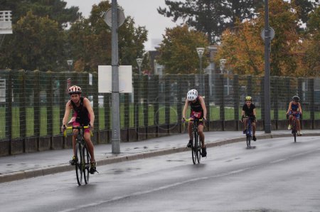 Téléchargez les photos : Reims, France - Octobre 2022 - Jeunes garçons en vêtements de sport à vélo de course, affrontant le triathlon du Stade de Reims sur une route mouillée, sous la pluie, devant l'Université, sur le campus Moulin de la Housse - en image libre de droit