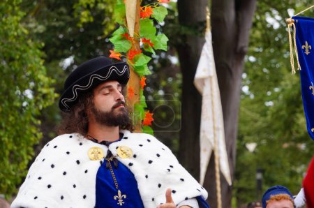 Téléchargez les photos : Reims, France - 28 mai 2022 - Comédien barbu se faisant passer pour le roi Charles VII, vêtu d'un manteau de couronnement bleu à col d'hermine et d'une fleur de lys royale, aux Fetes Johanniques de 2022" - en image libre de droit