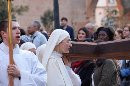 Téléchargez les photos : Toulouse, France - Mars 2023 - Une jeune religieuse catholique porte une croix de bois, tandis qu'un jeune moine porte une bougie, portant tous deux des soutènements blancs, lors d'une procession religieuse pour célébrer l'Annonciation - en image libre de droit