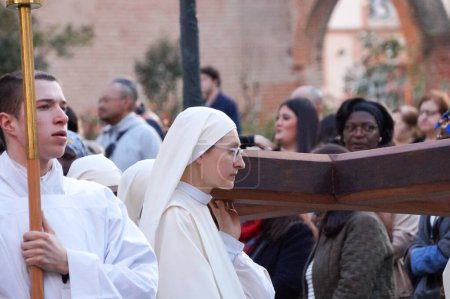 Foto de Toulouse, Francia - Marzo 2023 - Una joven monja católica lleva una cruz de madera, mientras que un joven monje lleva una vela, ambas con sotanas blancas, en una procesión religiosa en celebración de la Anunciación - Imagen libre de derechos