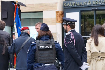 Foto de Toulouse, Francia - 24 de abril de 2023 - Por detrás, dos oficiales de policía, una capitana que lleva un chaleco antibalas y un comisionado con uniforme completo y cuarteto, asisten a una conmemoración oficial - Imagen libre de derechos