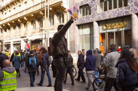 Foto de Toulouse, Francia - Feb. 2020- Un activista que distribuye un periódico de extrema izquierda y un manifestante que tiene un chaleco amarillo con una etiqueta que significa "Caminar (En Marche, partido de E. Macron) o morir, suficiente violencia estatal"" - Imagen libre de derechos