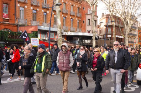 Photo for Toulouse, France - Feb. 2020 - Anarchist protesters in a demonstration of Yellow Vests and unions in Wilson Square against Emmanuel Macron's pension reform and social policy, waving a flag in skull - Royalty Free Image