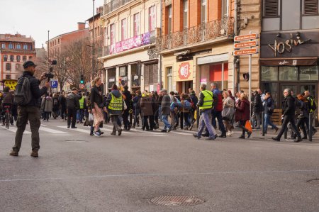 Foto de Toulouse, Francia - Feb. 2020 - Un periodista independiente equipado con una cámara de video en una barra y un micrófono filmando un desfile de chalecos amarillos (Gilets jaunes) protestando contra la reforma de las pensiones - Imagen libre de derechos