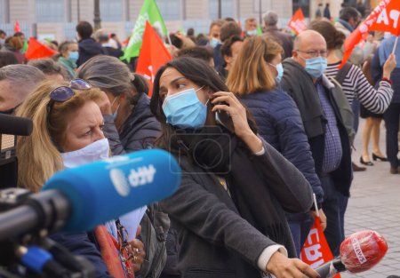 Foto de París, Francia - Oct. 2020 - Entre otros periodistas, una reportera del canal de televisión CNEWS, mientras sostiene un micrófono en una entrevista en vivo y lleva una máscara facial, está al teléfono y mira hacia atrás - Imagen libre de derechos