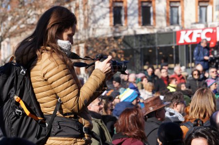 Foto de Toulouse, Francia - Feb. 2023 - Una joven fotógrafa de prensa tomando fotos y asegurando la cobertura de los medios en una manifestación dirigida por organizaciones de izquierda contra la reforma de las pensiones del gobierno - Imagen libre de derechos