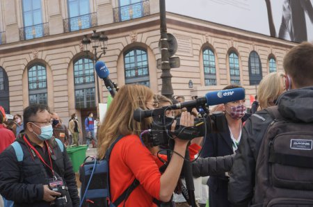Foto de París, Francia - 10 de octubre de 2020 - Entre otros colegas, una periodista de la Agencia Francesa de Prensa (AFP) opera una cámara de televisión equipada con un micrófono externo, en la acción de Marchons Enfants - Imagen libre de derechos