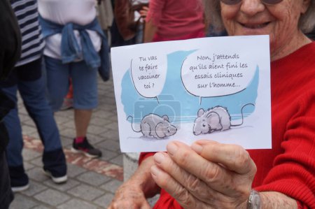 Photo for Albi, France - Aug. 7, 2021 - An elderly woman shows a cartoon featuring two laboratory mice discussing : "Do you plan to get vaccinated ? - No, I'm waiting for the end of clinical trials on Humans." - Royalty Free Image