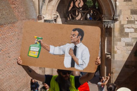 Téléchargez les photos : Albi, France - 7 août 2021 - Une caricature peinte sur une plaque en carton lors d'une manifestation contre le mandat de vaccination et le passeport sanitaire montre le président Emmanuel Macron pulvériser un pesticide RoundUp - en image libre de droit