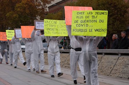 Photo for Albi, France - Nov. 2021 - Demonstrators in hospital white coats, wearing masquerade masks, take to the streets in the city centre with placards, to expose Covid-19 restrictions and vaccine mandates - Royalty Free Image
