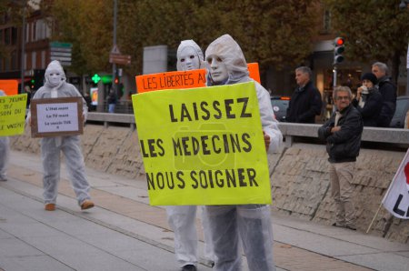 Photo for Albi, France - Nov. 2021 - Demonstrators in hospital white coats, wearing masquerade masks, take to the streets in the city centre with placards, to expose Covid-19 restrictions and vaccine mandates - Royalty Free Image