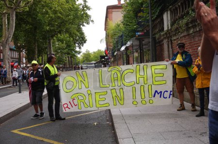 Foto de Albi, Francia - 31 de julio de 2021 - Manifestantes que se oponen al mandato de la vacuna y el pasaporte de salud ("pase verde") despliegan una pancarta que dice "Nunca nos rendiremos", al margen de la procesión principal. - Imagen libre de derechos