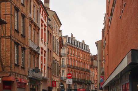Foto de Toulouse, Francia - Junio 2021 - La calle Rue de la Pomme en Capitole District, en la esquina con Rue d 'Alsace-Lorraine, bordeada de casas adosadas de ladrillo rosa, con el edificio Monoprix a la derecha - Imagen libre de derechos