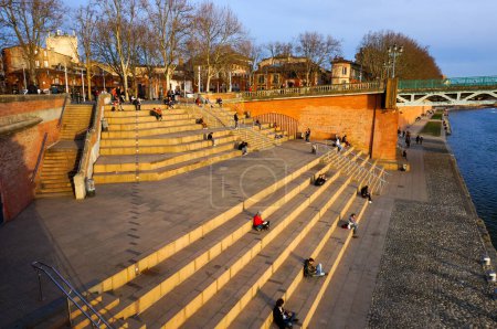 Téléchargez les photos : Toulouse, France - Février 2020 - Locaux et touristes profitant du coucher de soleil sur les escaliers de la célèbre place Saint-Pierre, sur le remblai de la Garonne, à côté du pont métallique - en image libre de droit