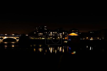 Téléchargez les photos : Night view of lights from the windows of the residential buildings of Bazacle Promenade Dike, in Toulouse, France, and Pont des Catalans Bridge crossing the river Garonne with reflection in the water - en image libre de droit